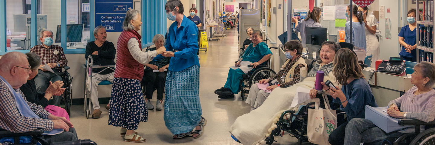 Two patients greet each other in a medical facility as others smile and interact