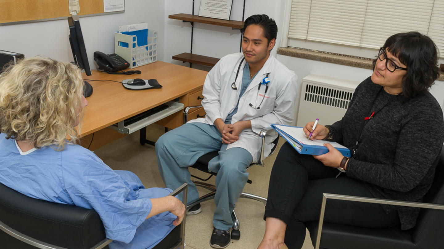 Two doctors are seated talking with a patient who is also seated