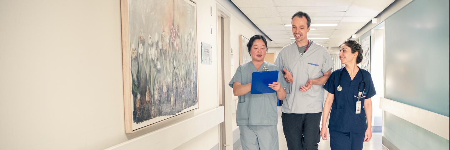 Three people walk down a hallway as they talk and review information on a clipboard