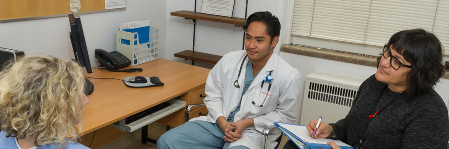 Two doctors are seated talking with a patient who is also seated