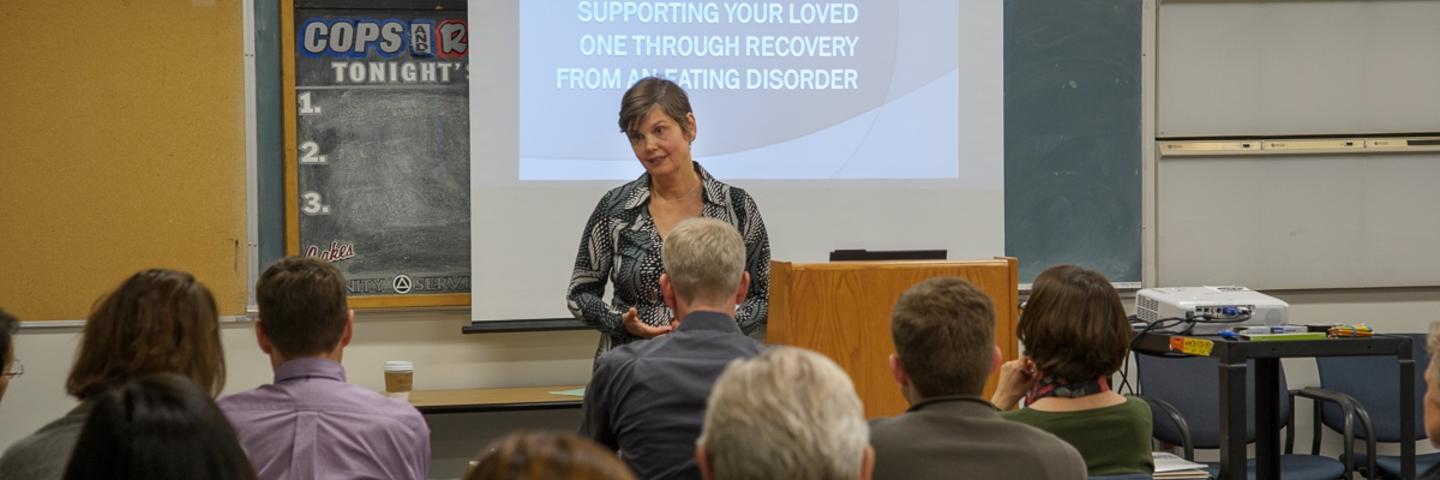 A women in front of a screen speaking to a group of people