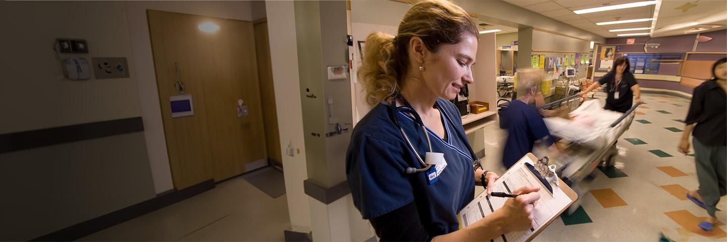 Nurse filling out a medical form as a patient on a hospital bed is being moved to another room.