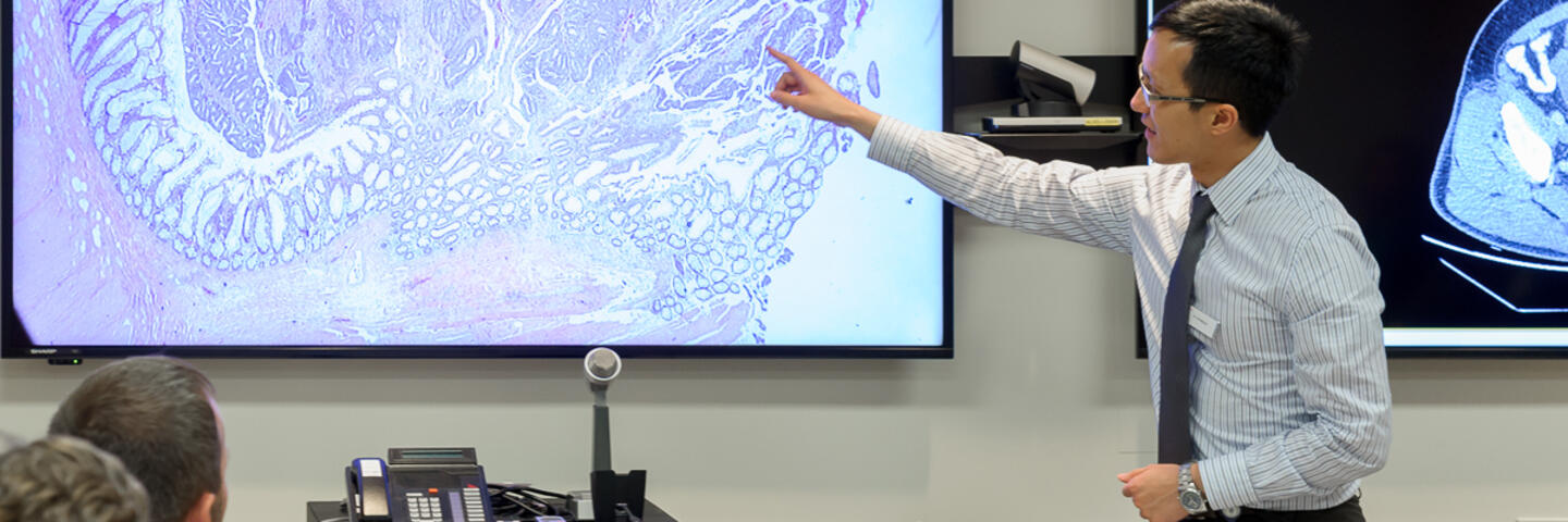 A man stands in front of a projector screen